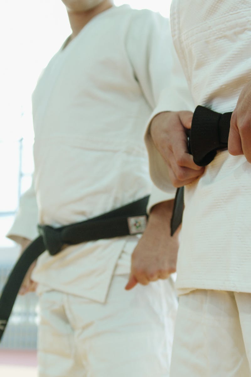 Two martial artists in white uniforms holding black belts, showcasing discipline and strength.